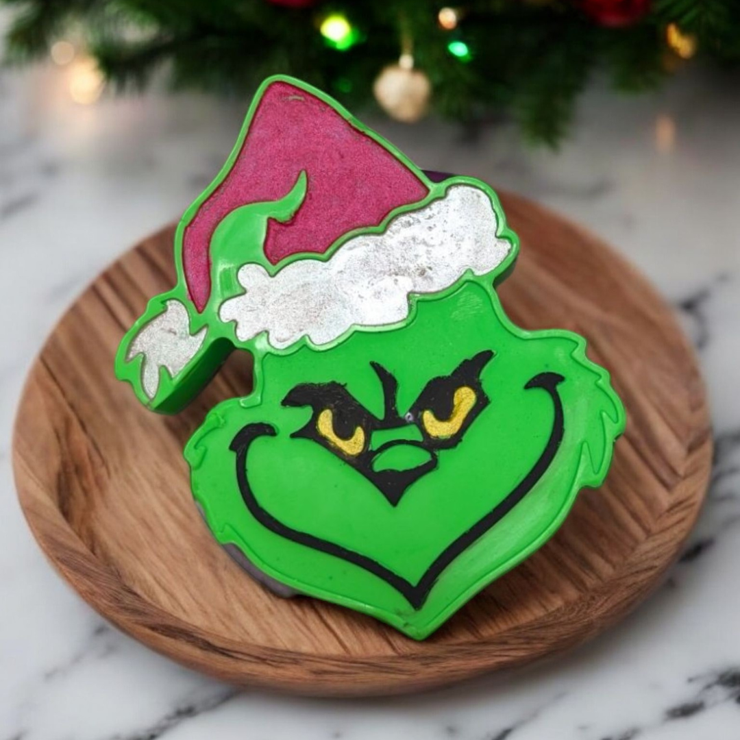 Grinch-shaped handmade soap on a wooden plate with Christmas tree in the background