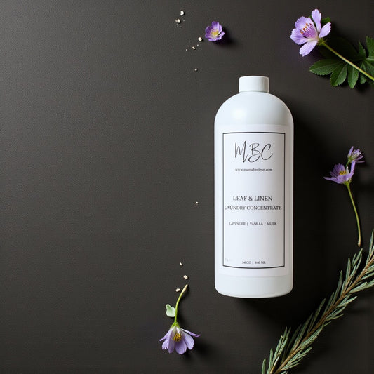 White bottle of MBC Leaf & Linen Laundry Concentrate on a dark background with flowers.