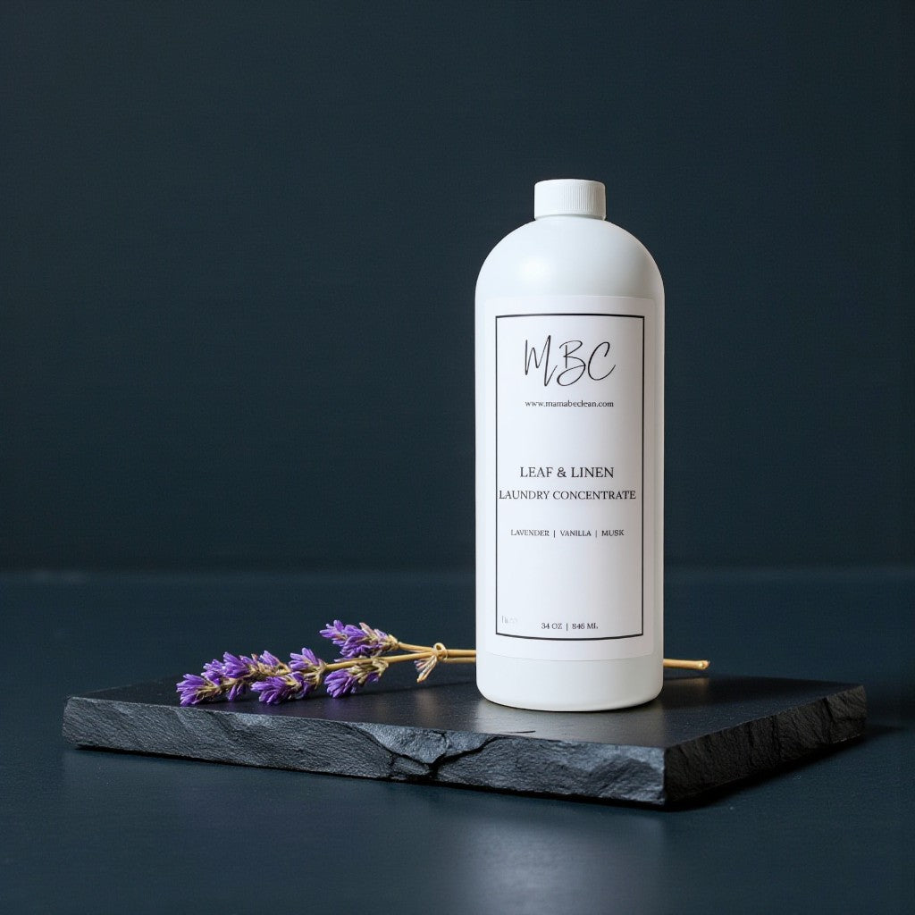White bottle of MBC Leaf & Linen Laundry Concentrate on a dark surface with lavender flowers.