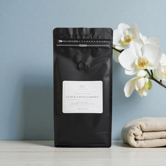 Black laundry detergent bag with a label, white orchid, and folded beige towel on a light blue background