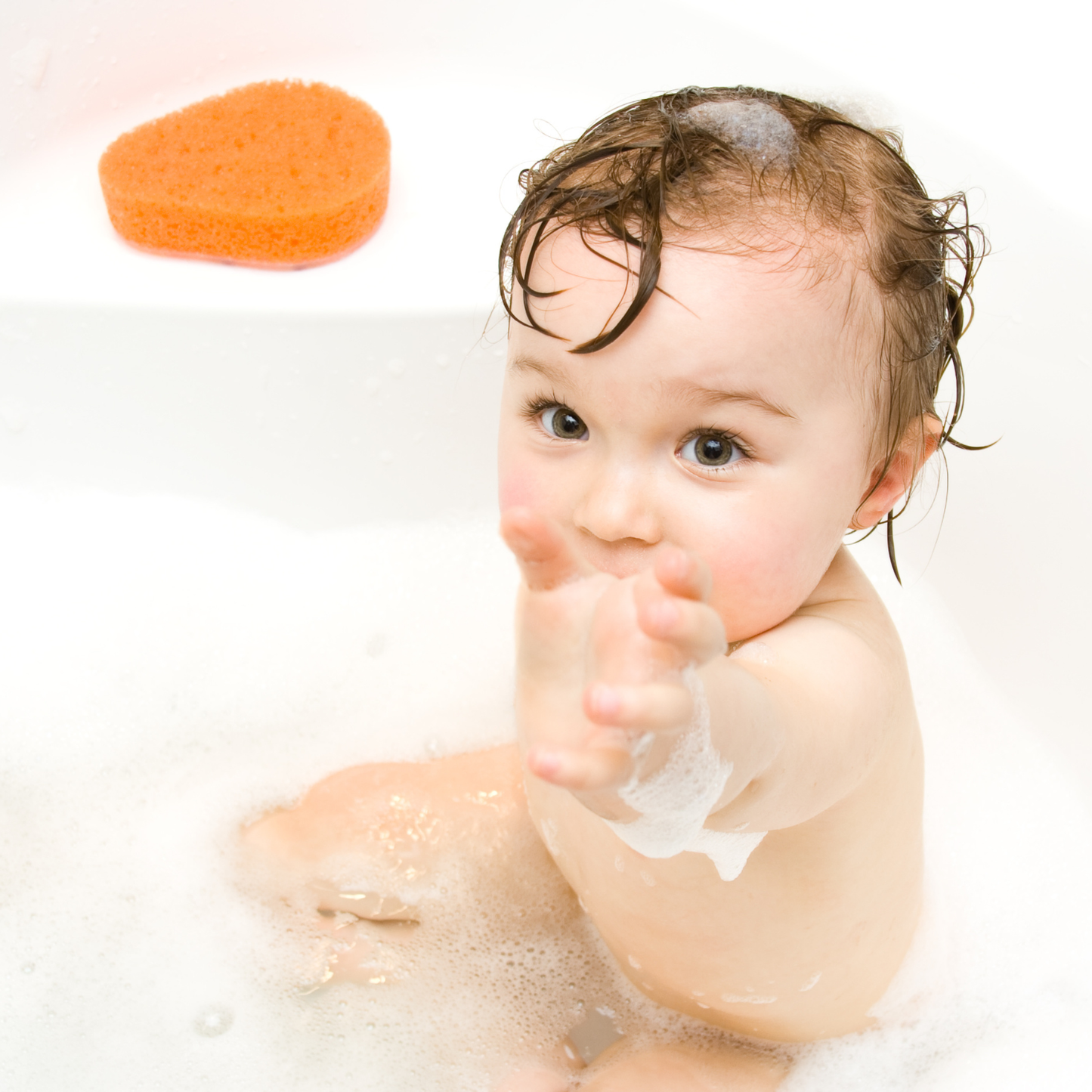 Baby with soap bubbles in a bath, with an orange sponge in the background