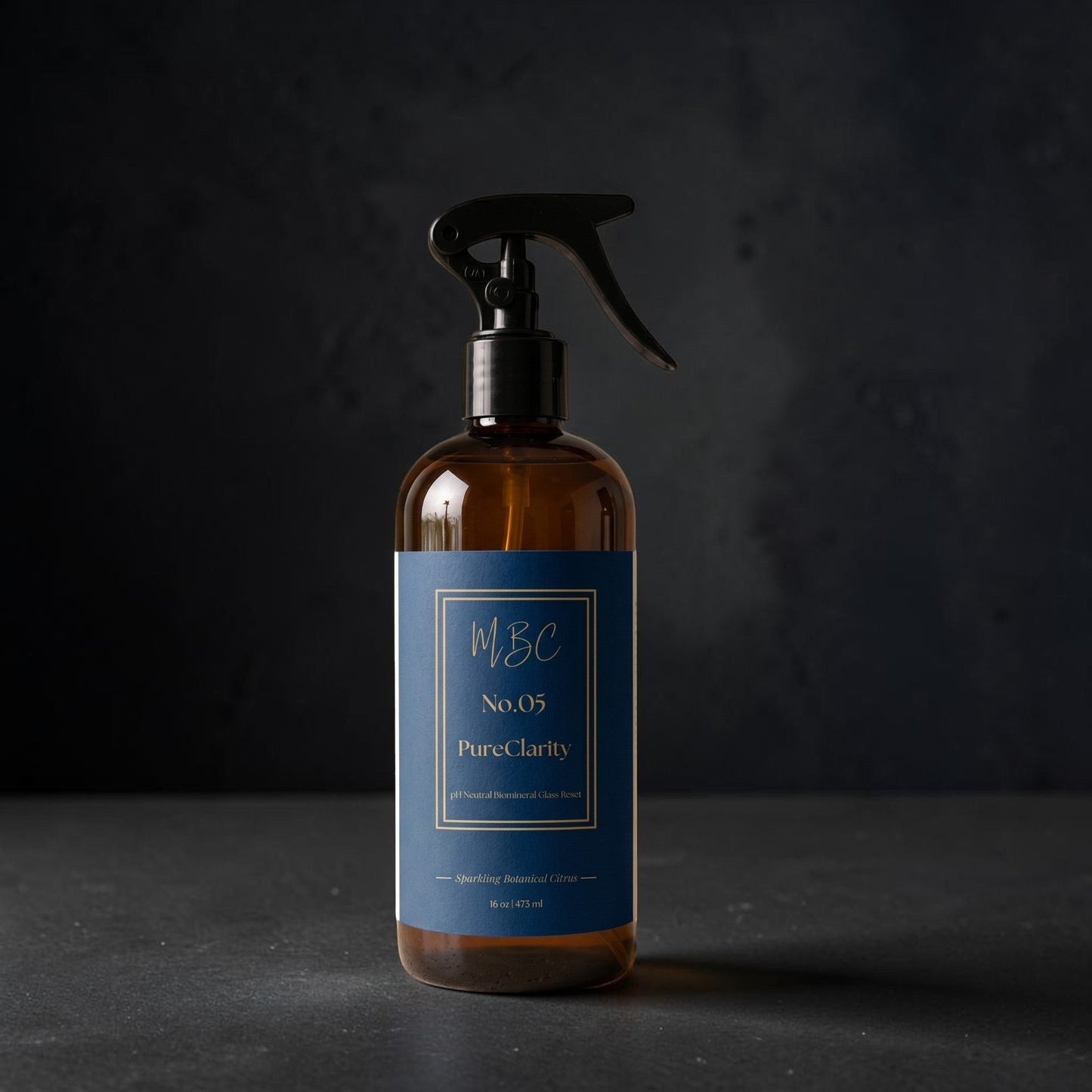 Mama Be Clean PureClarity glass cleaner in an amber spray bottle with a navy blue label on a dark surface.