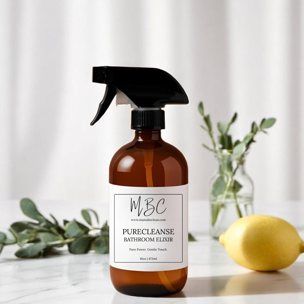 Brown spray bottle labeled 'MBC PureCleanse Bathroom Elixir' on a white surface with a lemon and eucalyptus leaves.