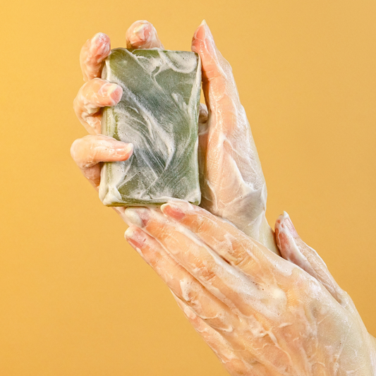 Hand holding a green soap bar against a yellow background